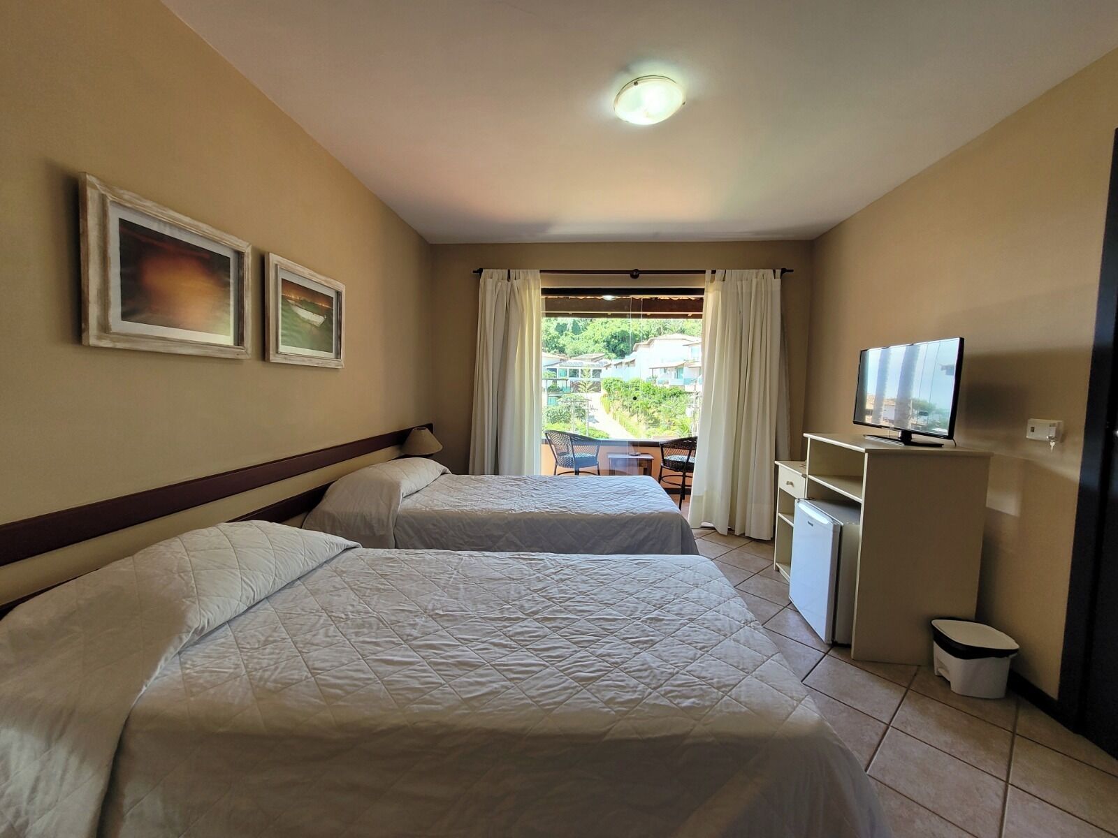 A hotel room with two beds, a TV, a desk, and a view of the outdoors.