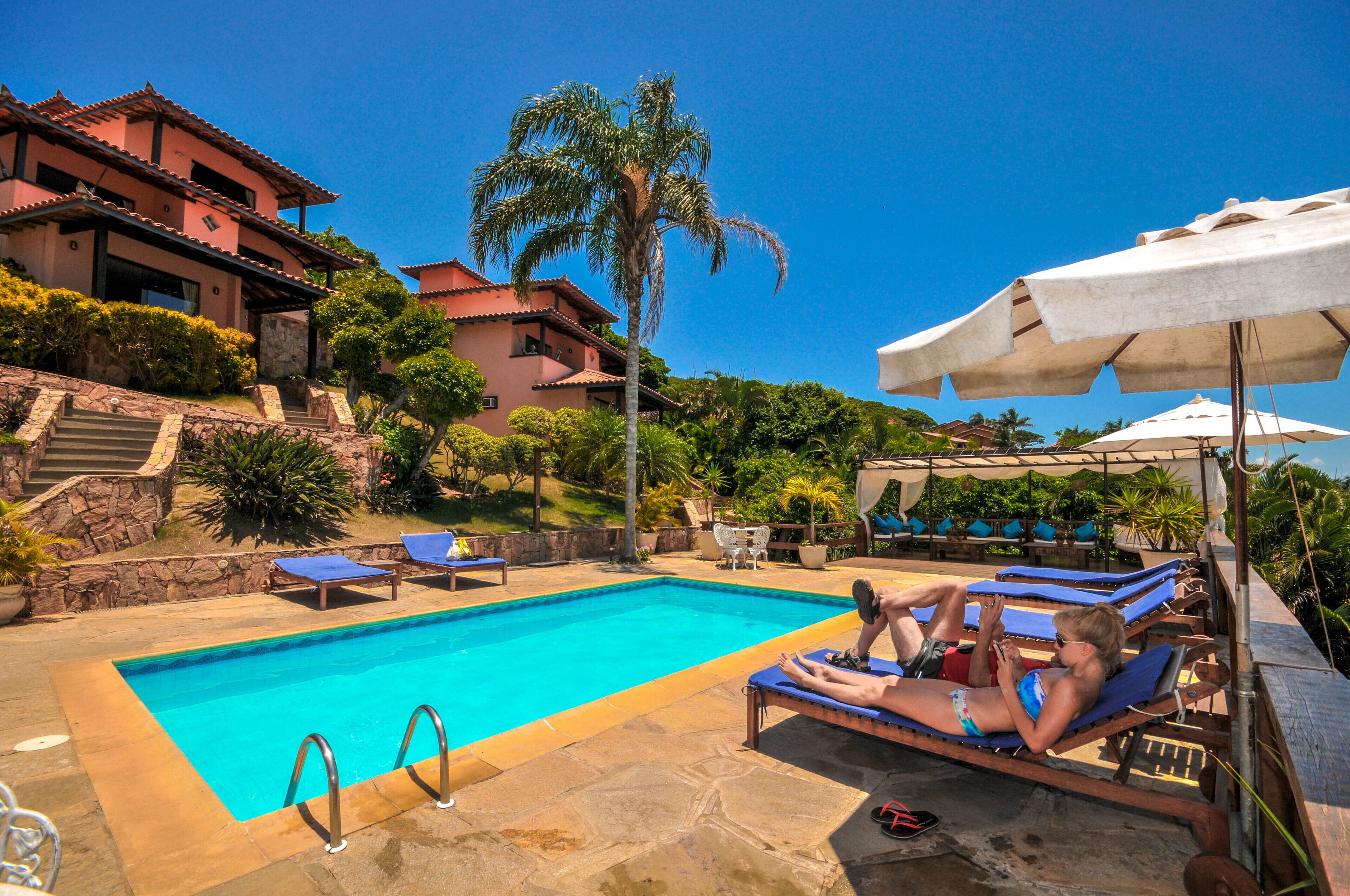 A swimming pool with lounge chairs and umbrellas, surrounded by a landscaped garden and a large house.