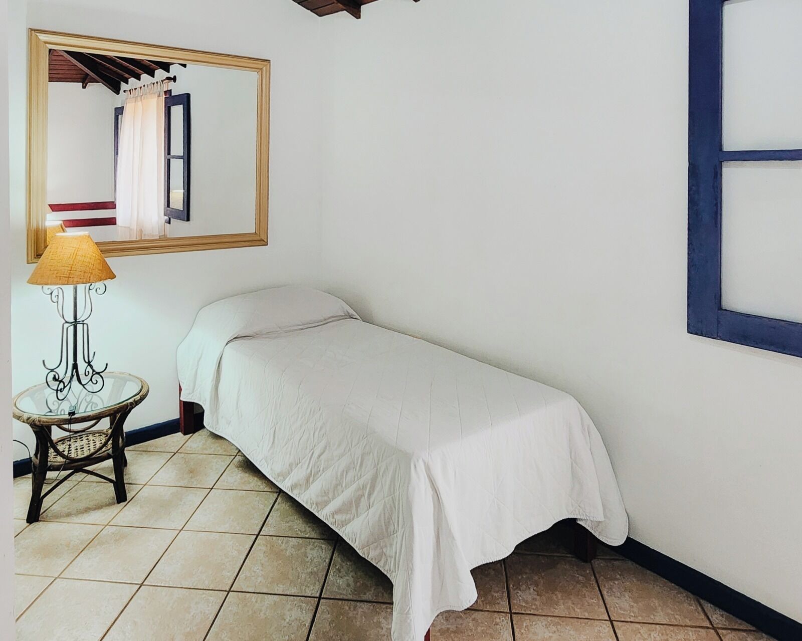 A small, single-bed room with a bed, a nightstand, a lamp, and a mirror on the wall.