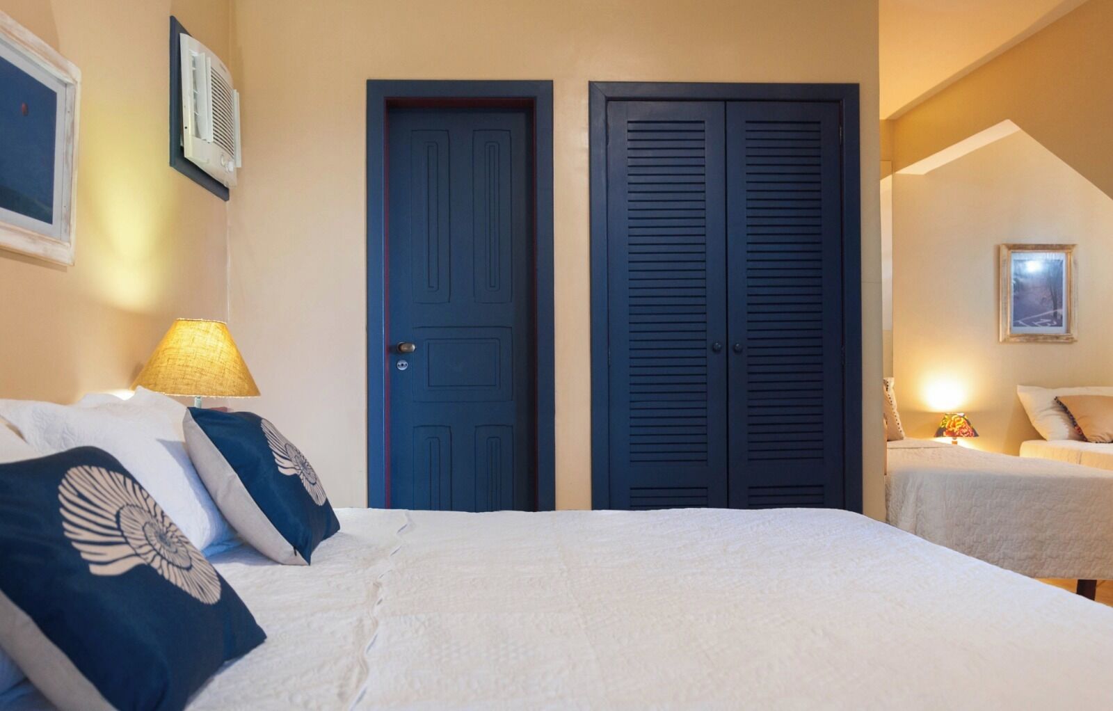 A bedroom with a bed, two doors, a lamp, and a painting on the wall.