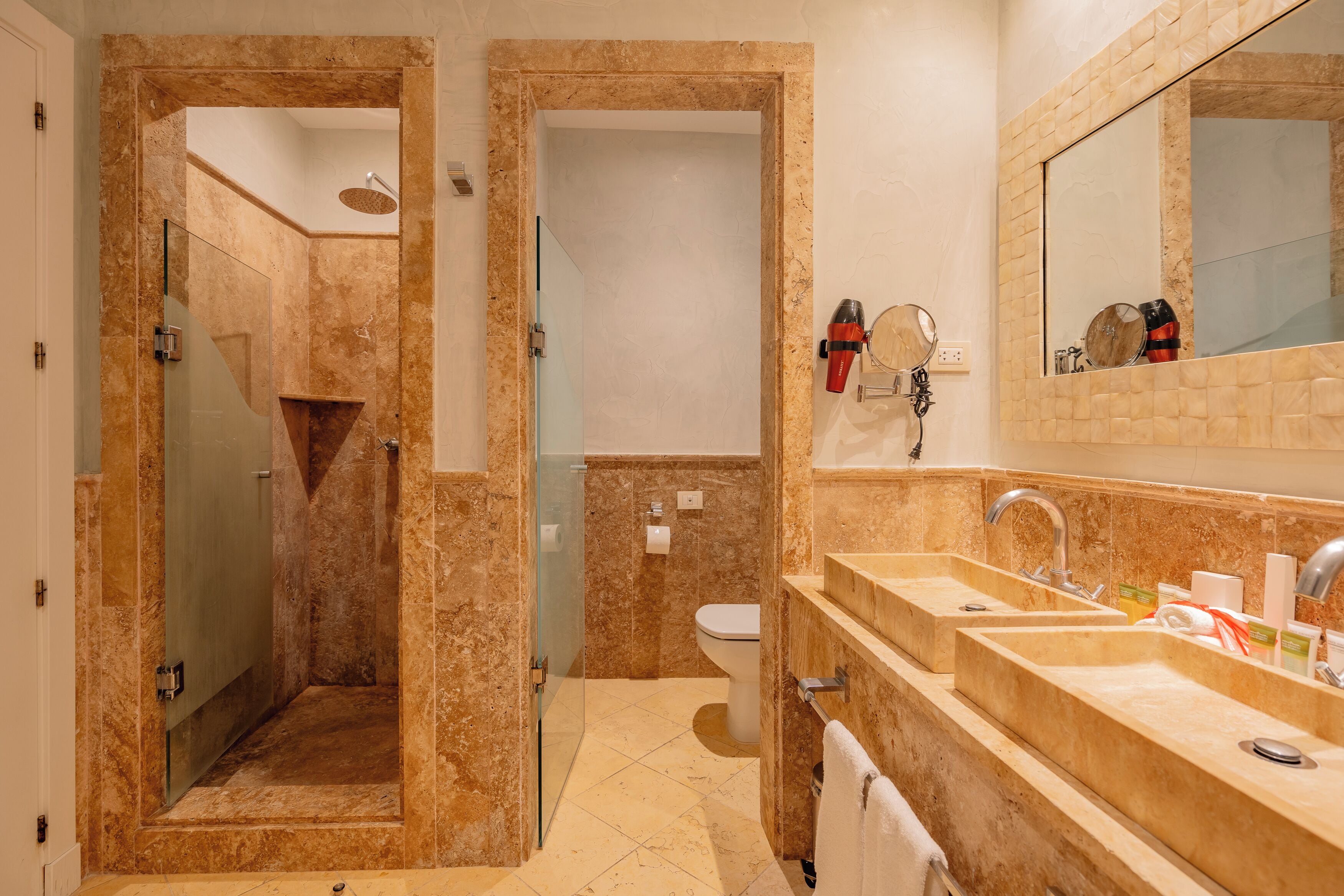 A bathroom with a glass shower enclosure, a toilet, and a double sink with a large mirror above.