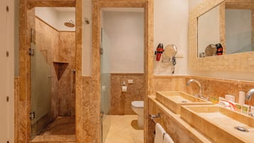 A bathroom with a glass shower enclosure, a toilet, and a double sink with a large mirror above.
