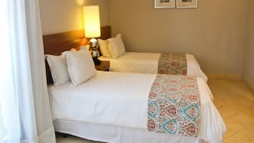 Una habitación de hotel con dos camas, una mesita de noche con lámpara y dos cuadros en la pared.