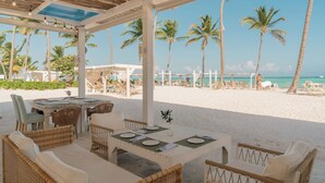 Un restaurant situé en bord de mer, avec une terrasse, des palmiers et une vue sur l’océan.