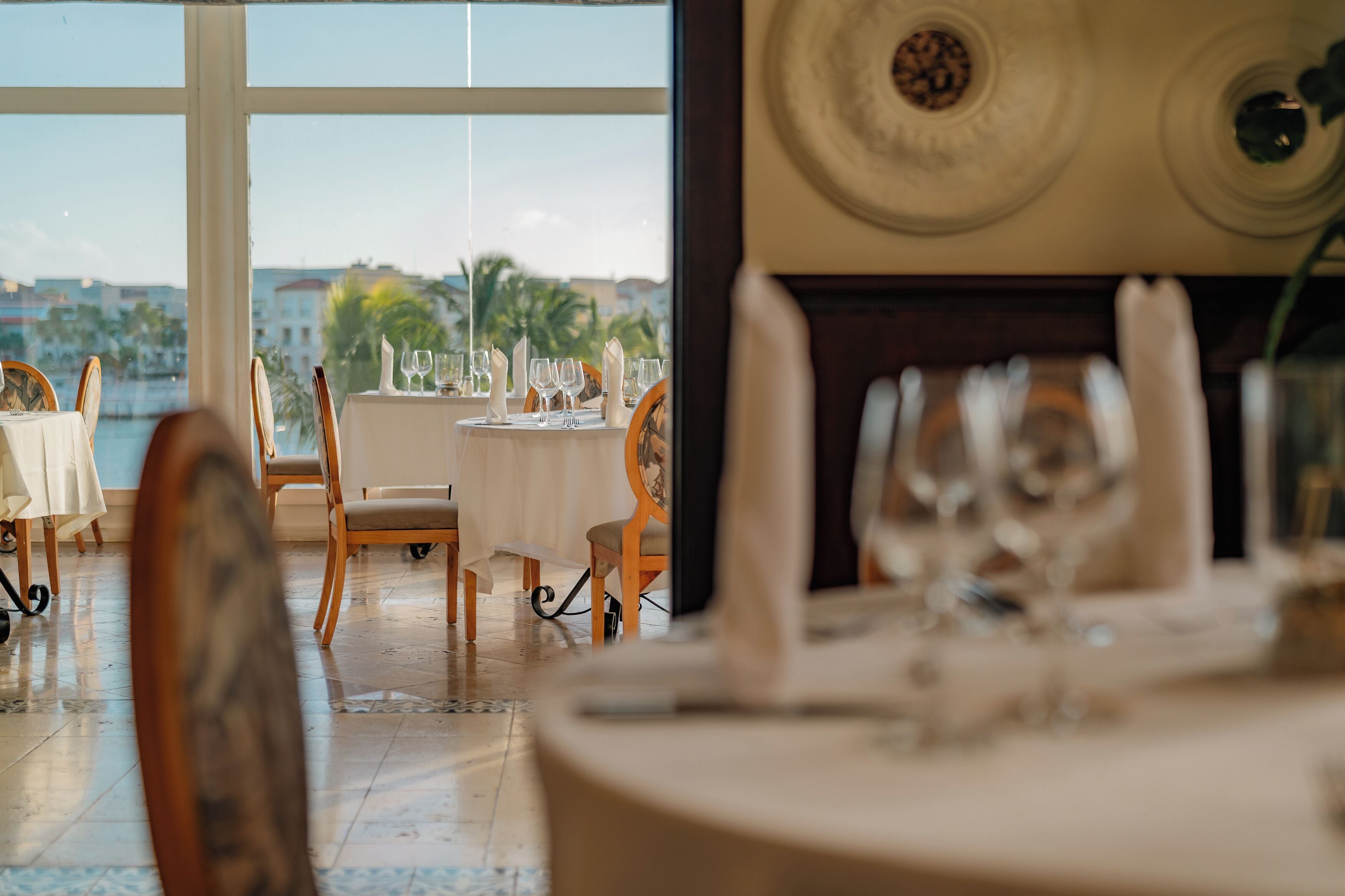 A dining area with tables set for a meal, chairs, and a view of the sea.
