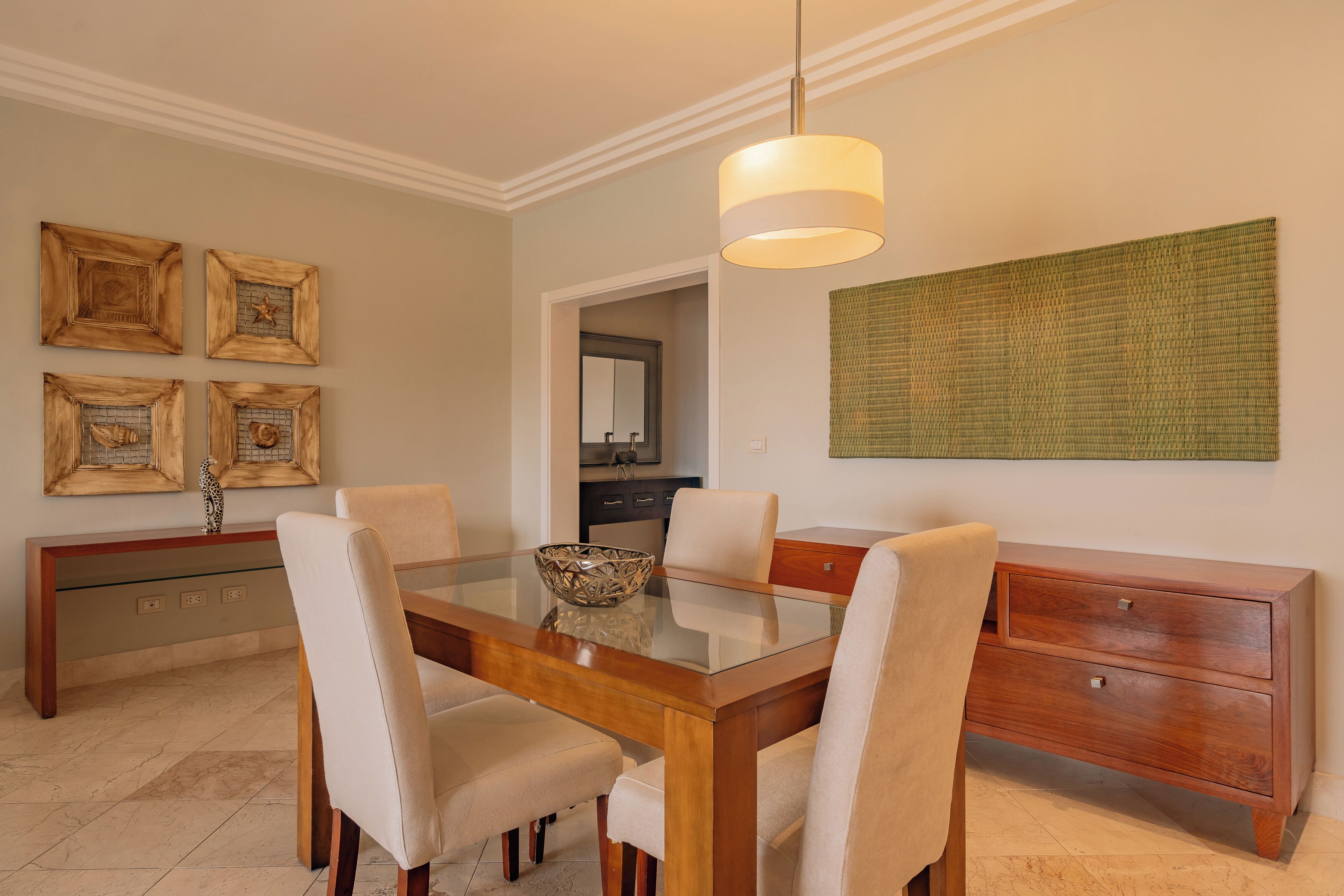 A dining area with a glass table, four chairs, a wooden sideboard, and a hanging light fixture.