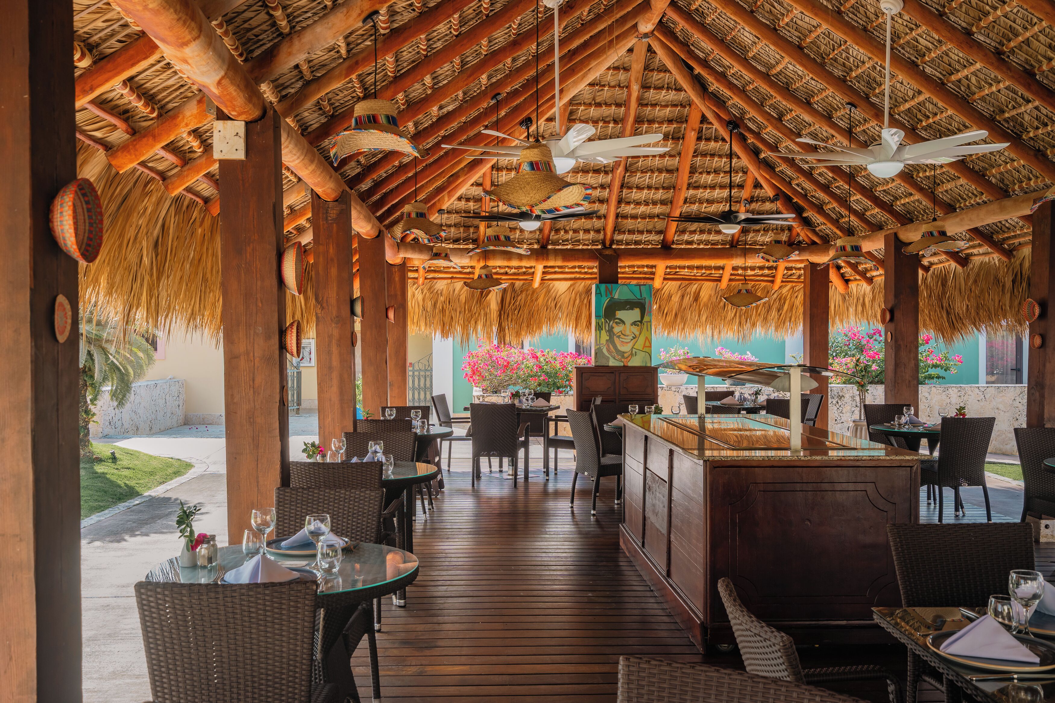 An outdoor restaurant with wooden tables and chairs, a thatched roof, and hanging decorations.
