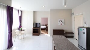 A modern hotel room with a dining area, a TV, a refrigerator, and a bed with a pink headboard.