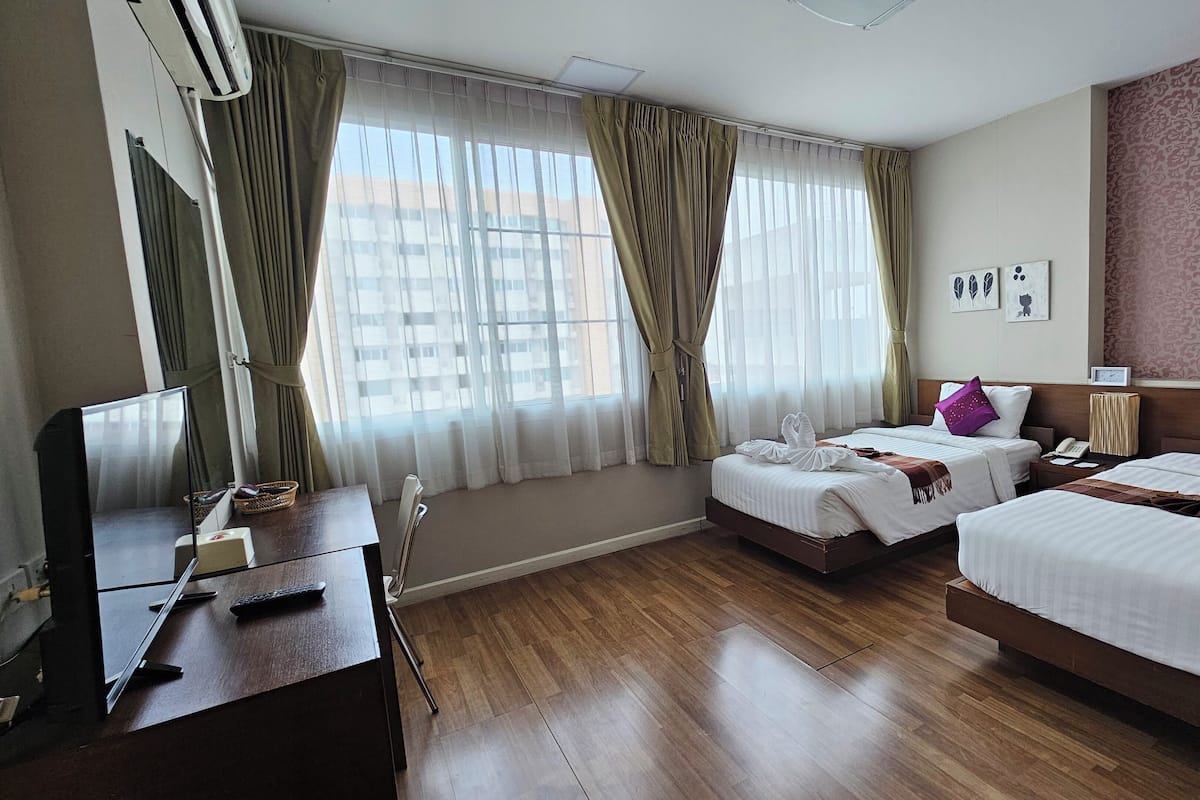 Une chambre d’hôtel avec deux lits, un bureau équipé d’un ordinateur et d’un téléphone, et une fenêtre avec des rideaux.