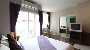 A hotel room with a bed, a TV, an air conditioner, and a view of the outside.