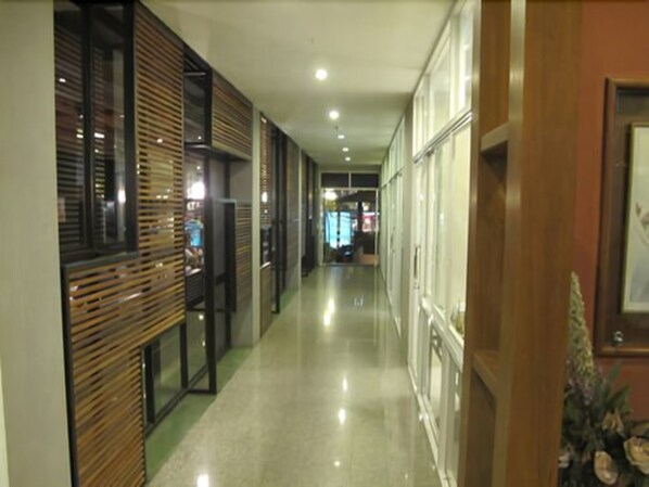 A hallway with wooden paneling and glass doors, leading to a room with a bed and a nightstand.