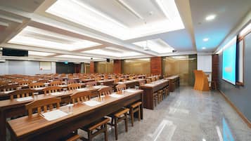 A conference room with rows of wooden tables and chairs, a large screen, and a projector.