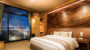 Una habitación de hotel con un ventanal grande, una cama con cabecera de madera, una mesita de noche y un armario.