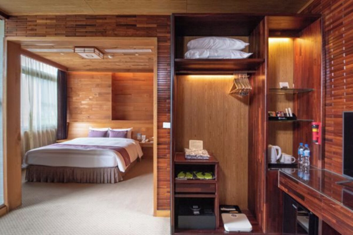 A hotel room with a bed, a wooden wall, a shelf with toiletries, and a television.