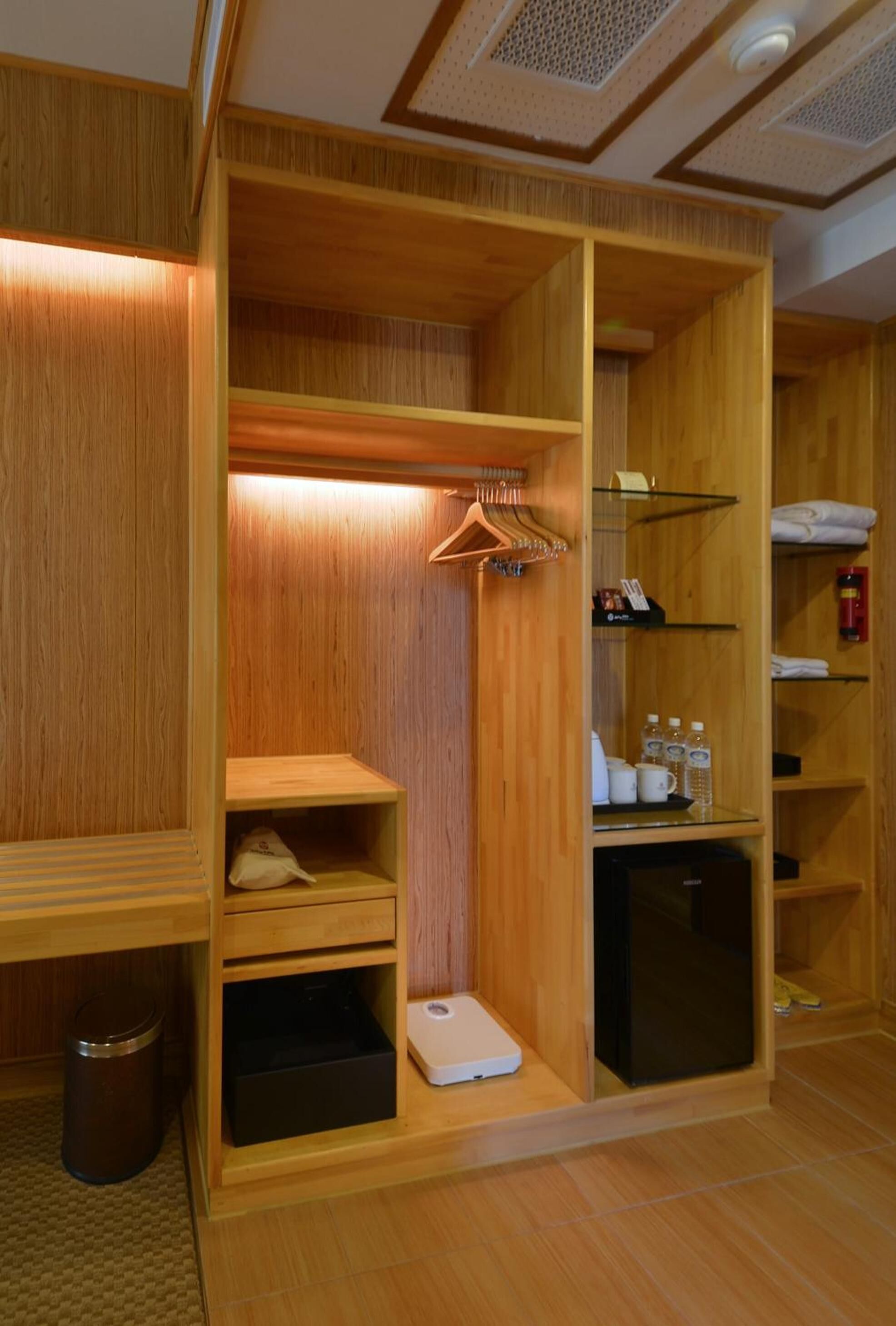A wooden room with a built-in wardrobe, a small refrigerator, and a shoe rack.