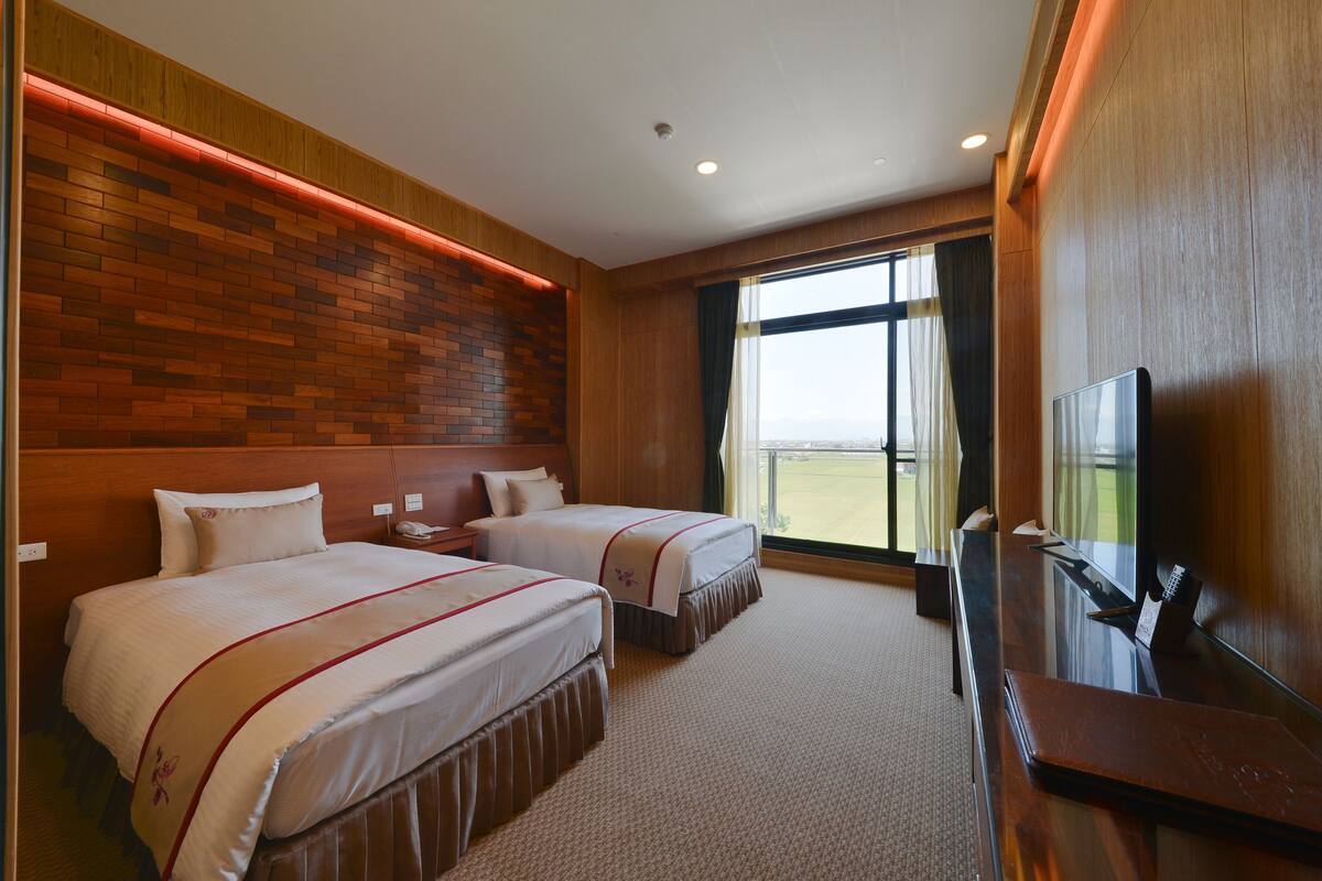 A hotel room with two beds, a TV, and a large window with a view.