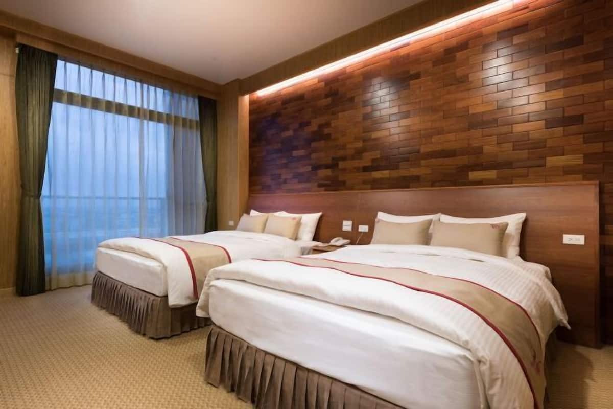 A hotel room with two beds, a wooden headboard, a large window with curtains, and a carpeted floor.