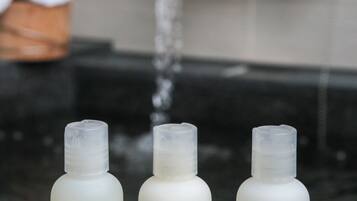 Tres botellas de Hinoki Shandori Spa sobre una superficie de piedra, con un grifo al fondo.