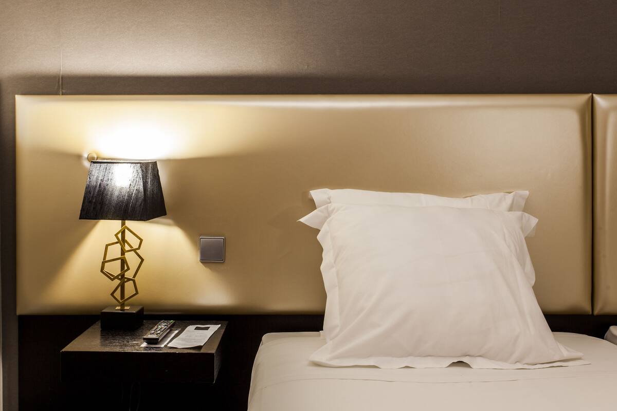 Un lit bien fait, avec un oreiller blanc et une lampe sur une table de chevet.