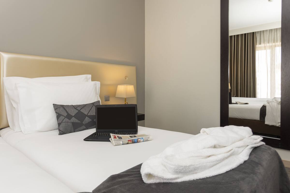 Une chambre d’hôtel avec un lit, un ordinateur portable, un magazine et une serviette blanche posée sur le lit.