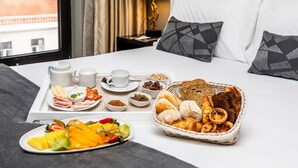 Ein ordentlich gedecktes Frühstücksbrett mit Gebäck, Brot und Früchten auf einem Hotelbett.