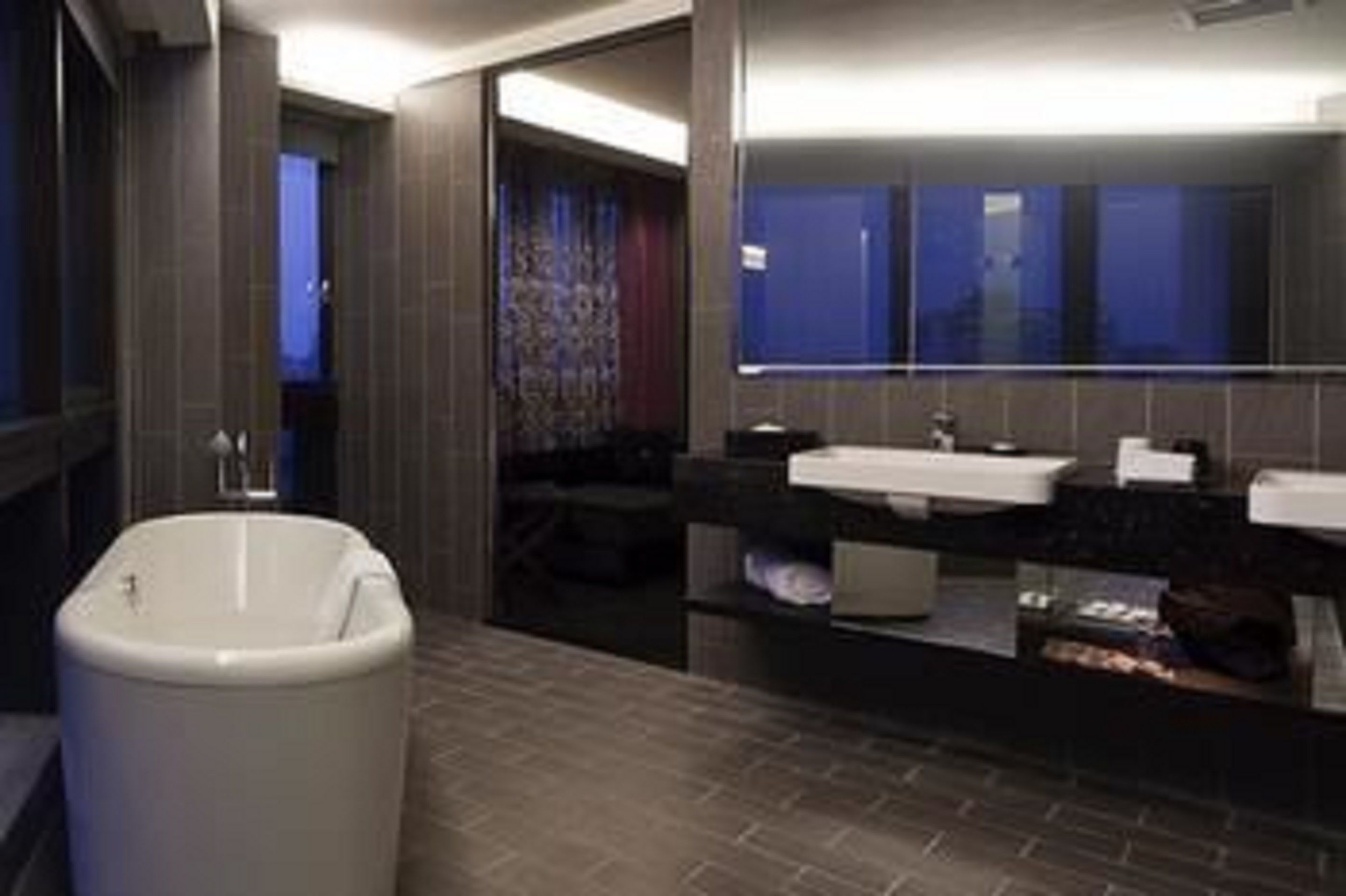 A modern bathroom with a freestanding bathtub, a large mirror, and a dark-toned vanity with a sink.