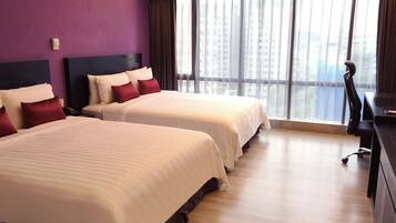 A hotel room with two beds, a desk, and a large window with a city view.