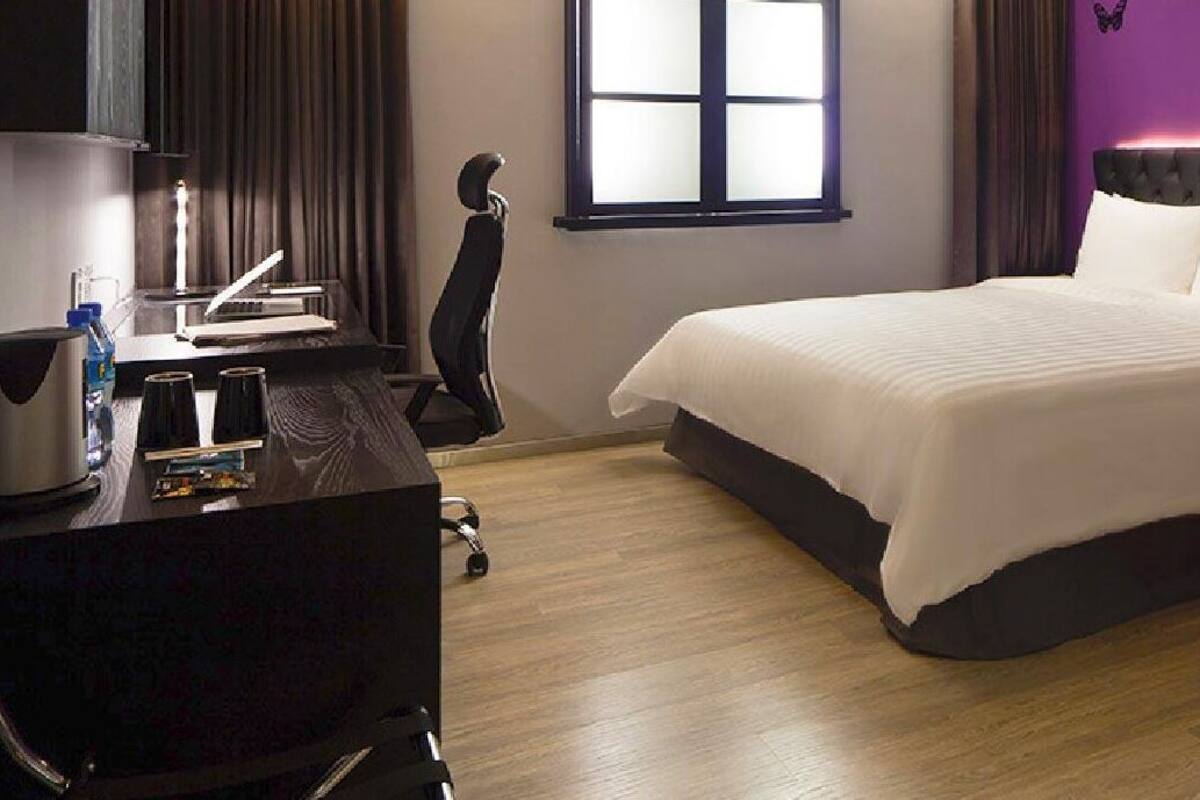 A hotel room with a bed, a desk, a chair, and a red armchair.