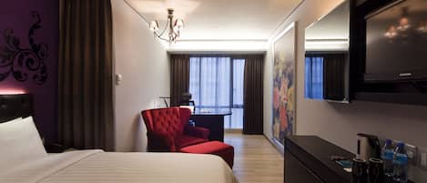 A hotel room with a large bed, a red armchair, a desk with a chair, a flat-screen TV, and a painting on the wall.
