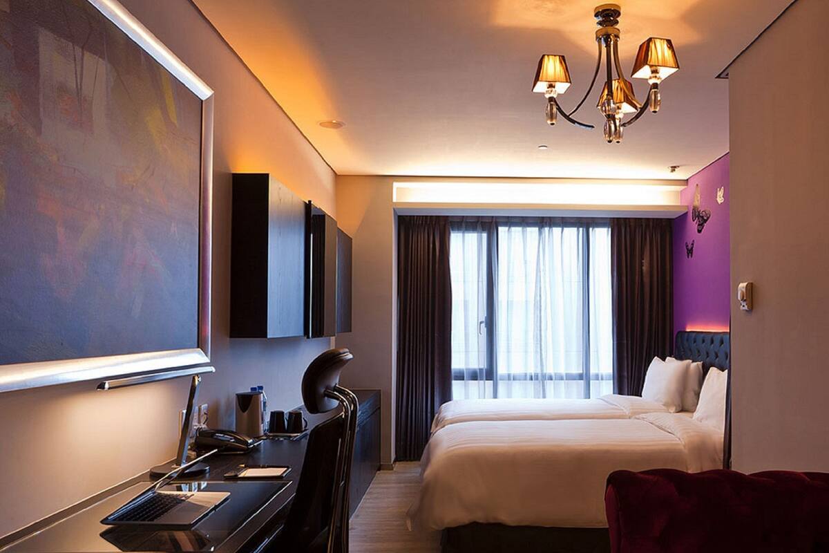 A hotel room with a bed, desk, chair, and a large window with curtains.