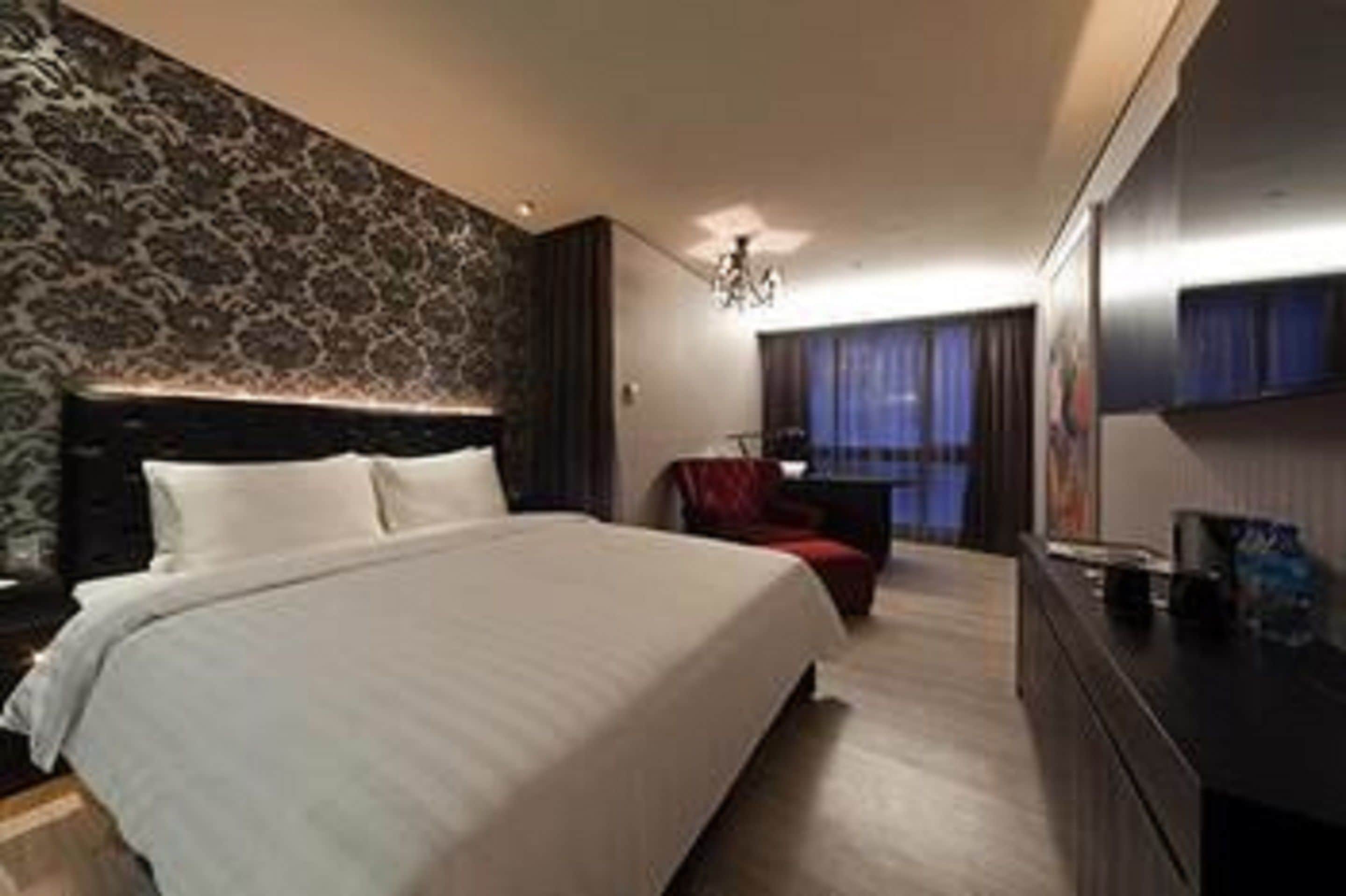 Una habitación de hotel moderna con una cama grande, un televisor de pantalla plana y una pared oscura con estampado.