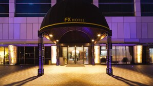 La entrada del Hotel FX, con un diseño moderno, que presenta una gran estructura en forma de cúpula y pilares iluminados.