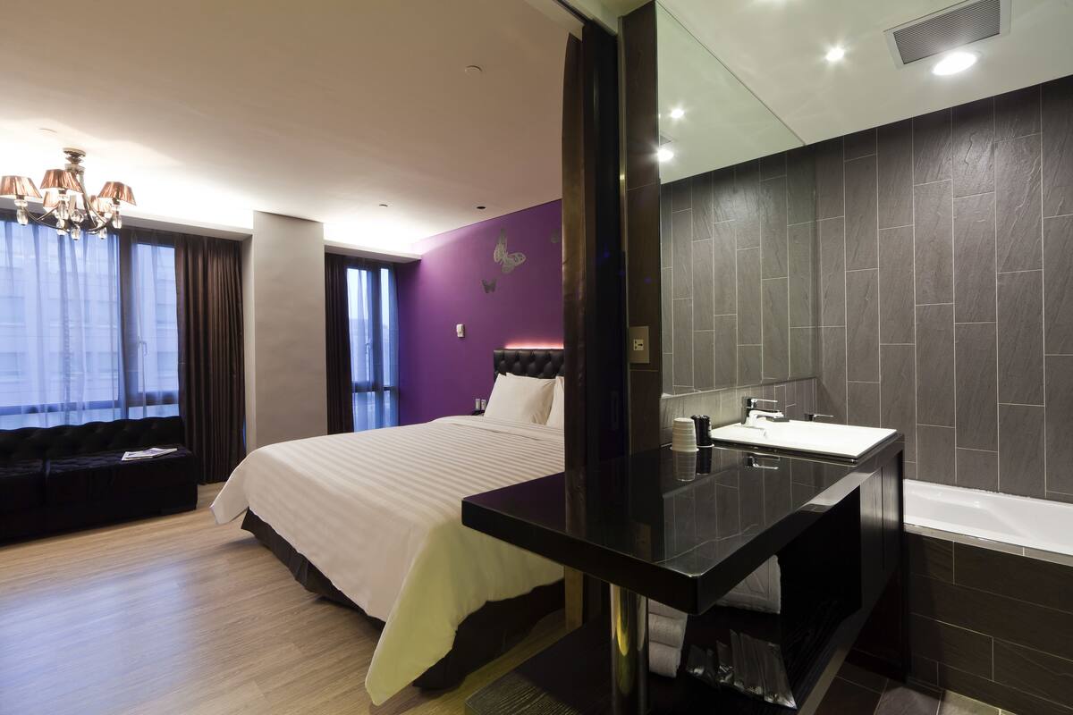 A modern hotel room with a large bed, a vanity with a mirror, and a bathtub.