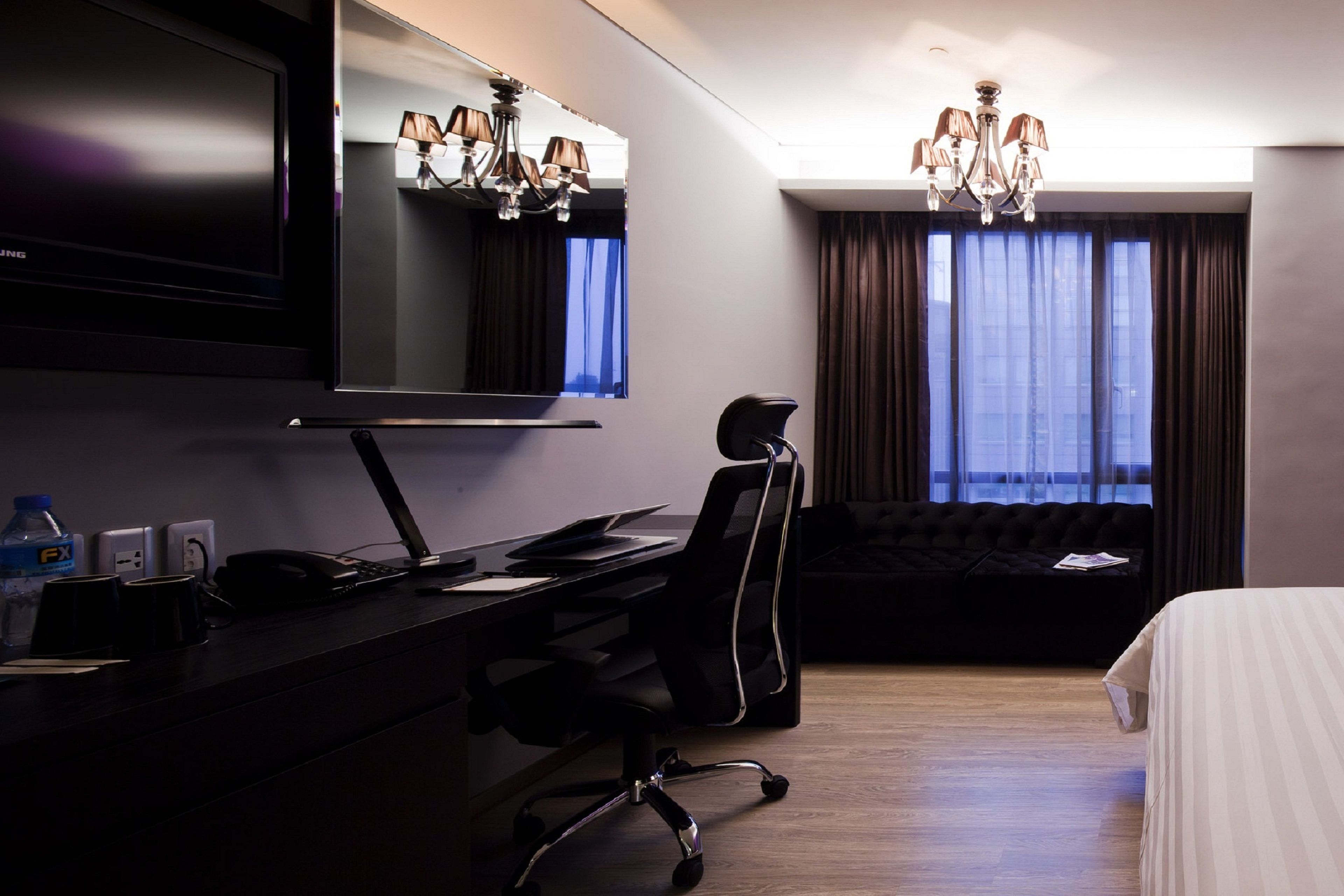 Habitación de hotel con escritorio, silla, cama y un ventanal con cortinas.