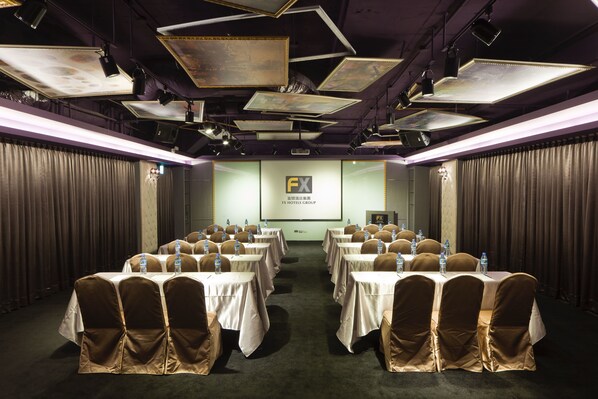 Una sala de conferències amb taules i cadires, ampolles d'aigua i una pantalla de projector que mostra "FX Hotels Group".
