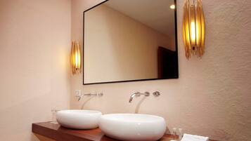 Un baño moderno con dos lavamanos blancos, un espejo grande y apliques de pared.