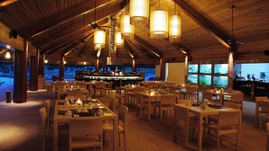 A spacious restaurant with high ceilings and wooden beams, featuring multiple dining tables and chairs, and a bar area visible in the background. - Bluewater Panglao Beach Resort (Panglao)