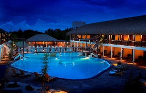A swimming pool with lounge chairs and a building with a thatched roof. - Bluewater Panglao Beach Resort (Panglao)