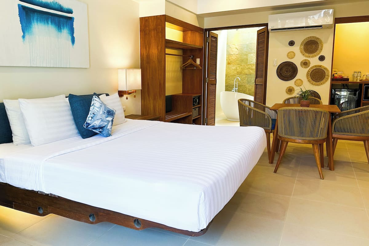 Habitación de hotel con una cama grande, mesitas de noche, un escritorio con sillas, un baño con bañera y una pared decorada con placas.