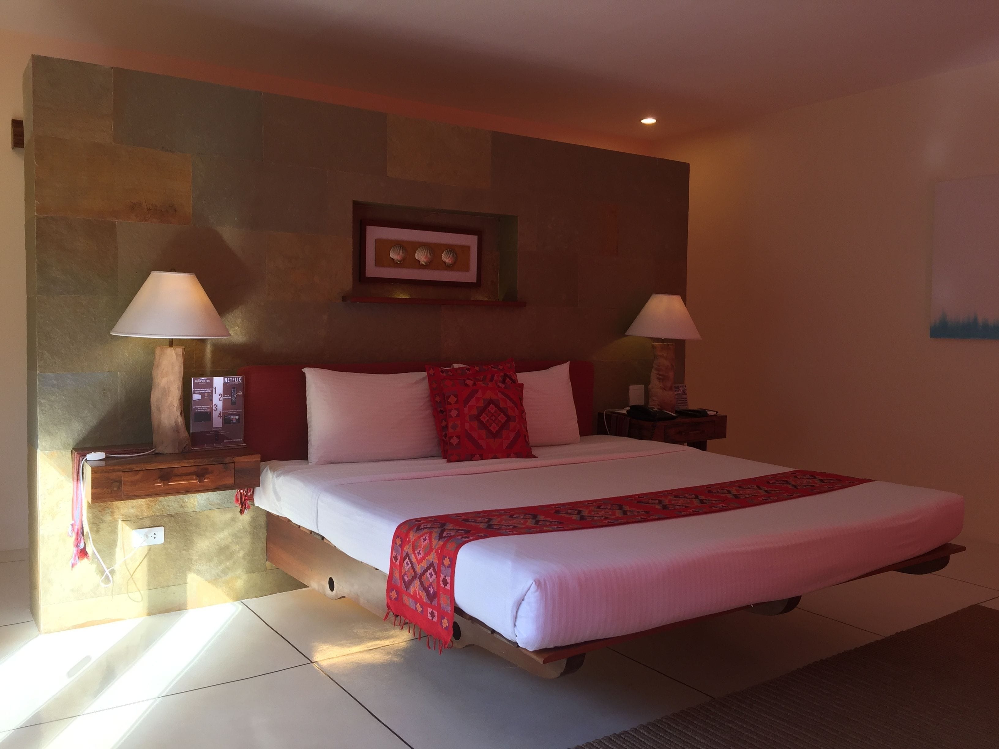 A hotel room with a large bed, two bedside lamps, a framed picture on the wall, and a wooden nightstand with a phone and a lamp.