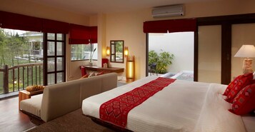 Habitación de hotel con una cama grande, un sofá, un escritorio y un balcón con vistas a zonas verdes.
