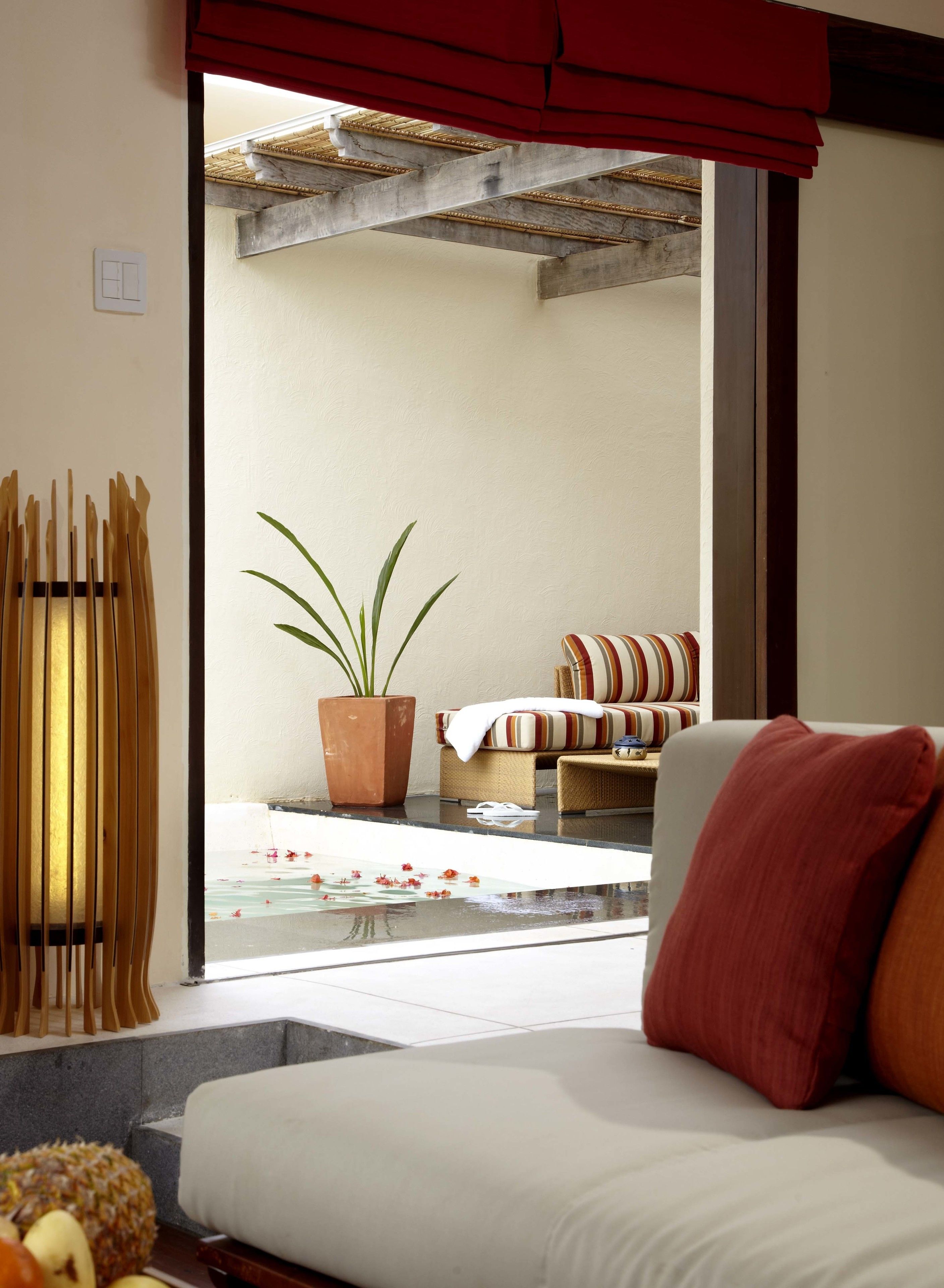 A modern living room with a sofa, a potted plant, and a view of an outdoor area with a pool and furniture.