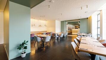 A modern dining area with multiple tables and chairs, a potted plant, and pendant lighting.