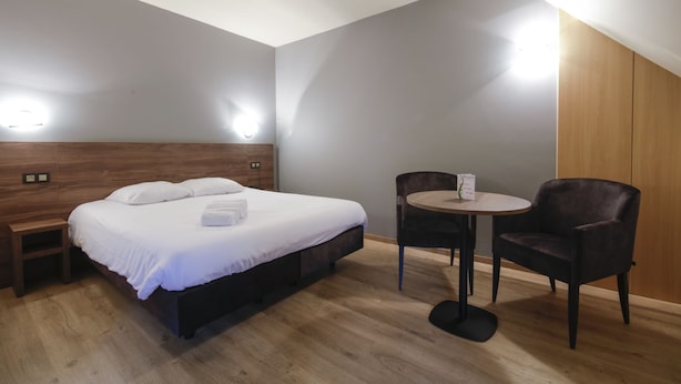 A bedroom with a bed, bedside table, chair, and a small round table. - Les Jardins de la Molignée (Anhée)
