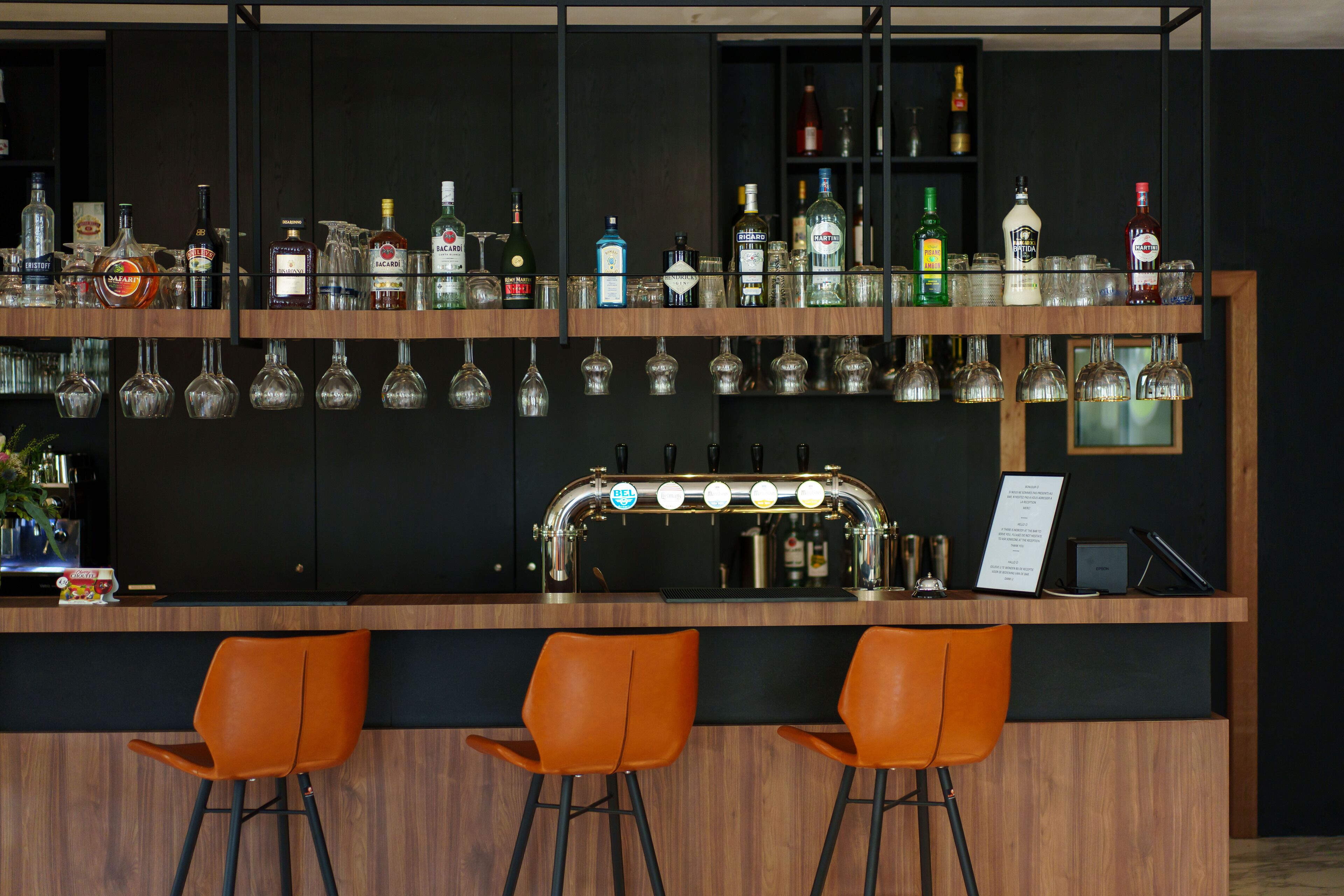 A bar area with a wooden counter, multiple liquor bottles, and orange bar stools.