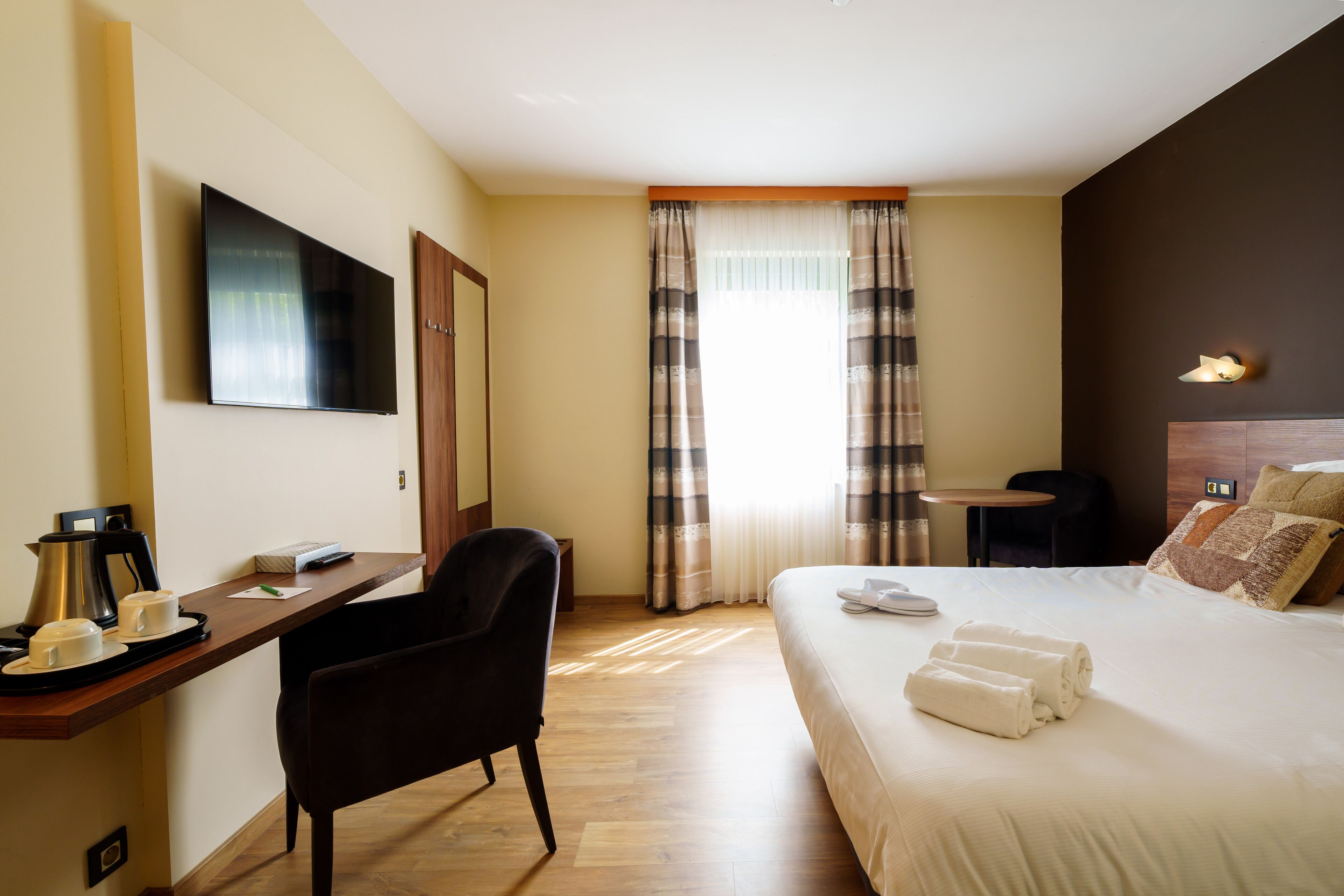 Une chambre d’hôtel comprenant un lit, un bureau avec une chaise, une télévision, une machine à café et une fenêtre avec des rideaux.
