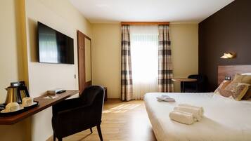 Une chambre d’hôtel comprenant un lit, un bureau avec une chaise, une télévision, une machine à café et une fenêtre avec des rideaux.