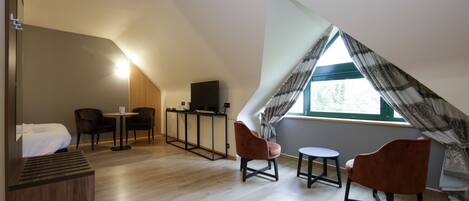 Habitación moderna y luminosa con techo inclinado, una cama, un escritorio, dos sillas y una ventana con cortinas.
