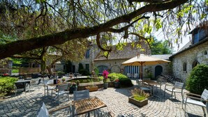 A courtyard with stone flooring, outdoor seating, and a large tree providing shade. - Les Jardins de la Molignée (Anhée)