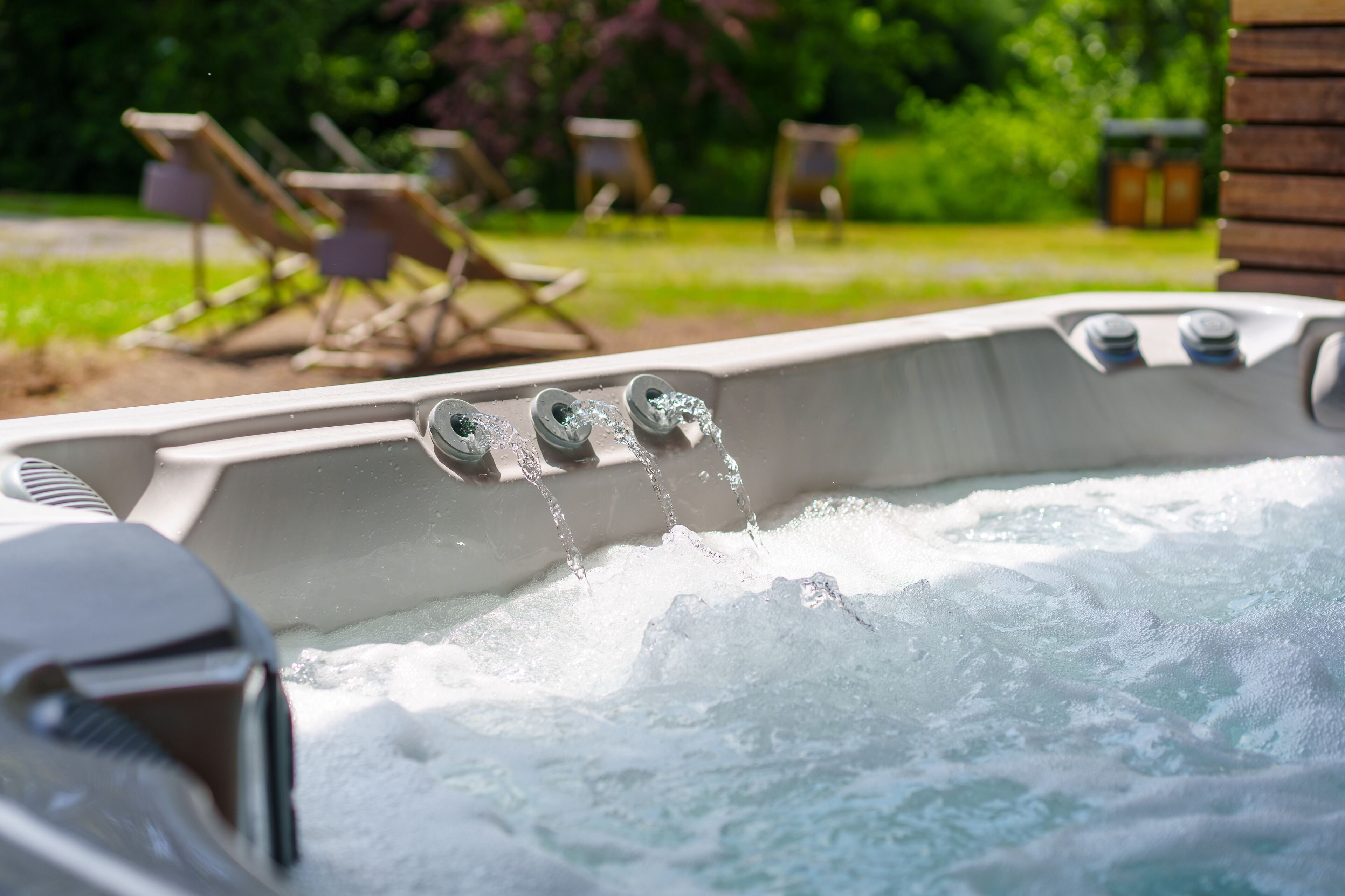 A hot tub with three jets of water, surrounded by outdoor furniture and greenery.